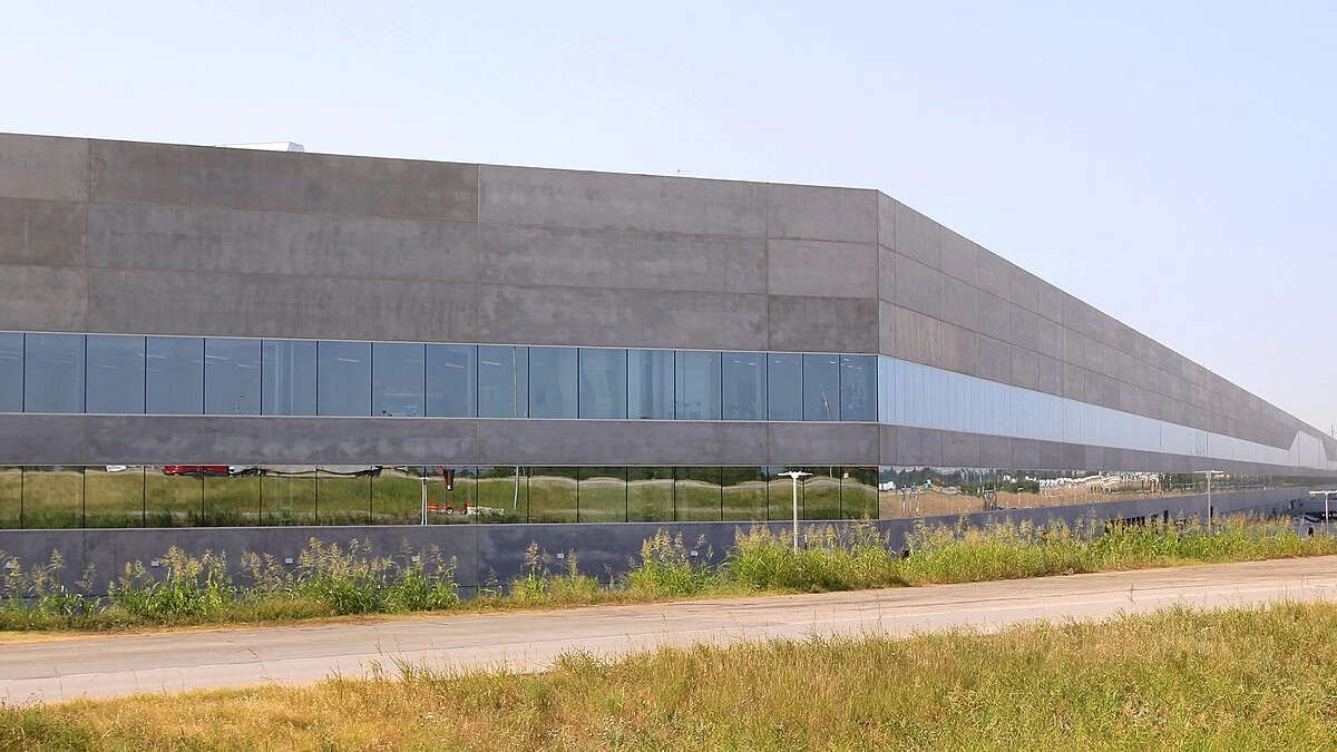 Exterior of Tesla Gigafactory Texas near Austin, with a large concrete factory facade and a glass-fronted lower level.