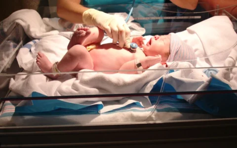 A doctor examines a newborn baby in a hospital bassinet.