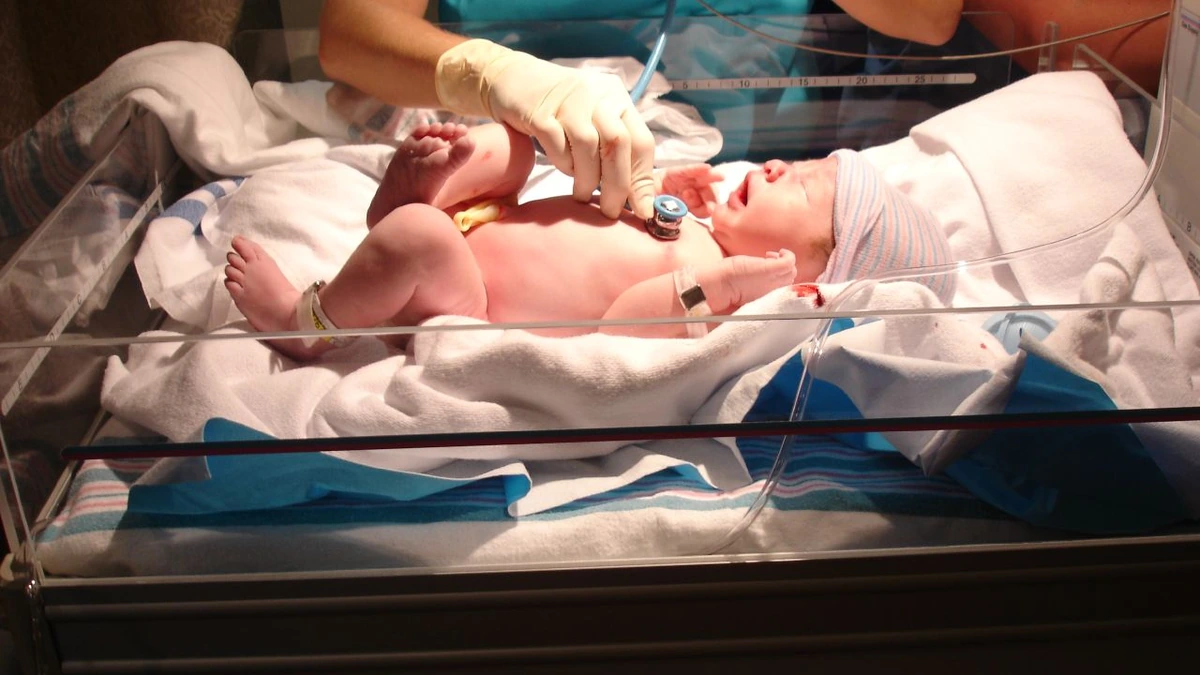 A doctor examines a newborn baby in a hospital bassinet.