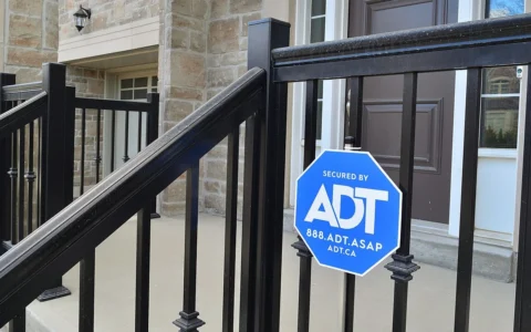 Blue ADT security sign mounted on a black metal railing outside a home.