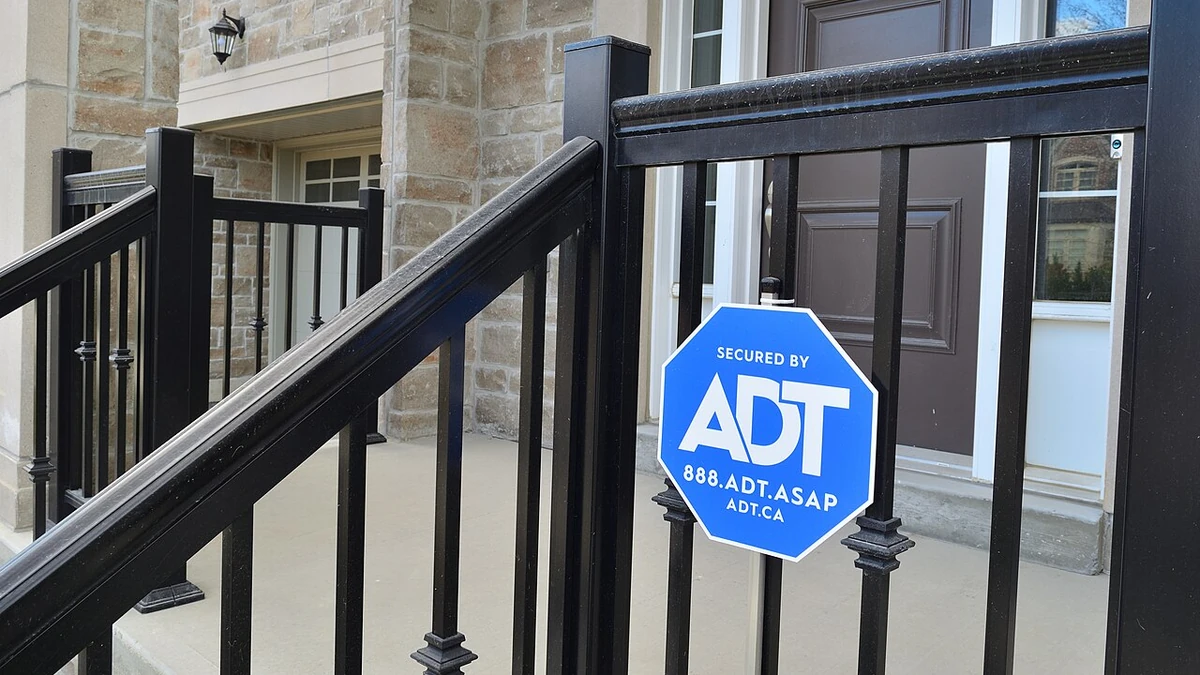 Blue ADT security sign mounted on a black metal railing outside a home.