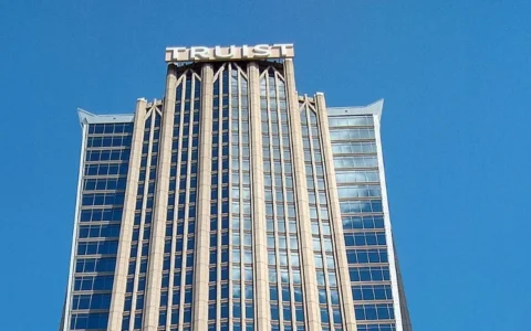 Top of Truist Center in Charlotte, North Carolina, with TRUIST lettering above its tower against a blue sky.