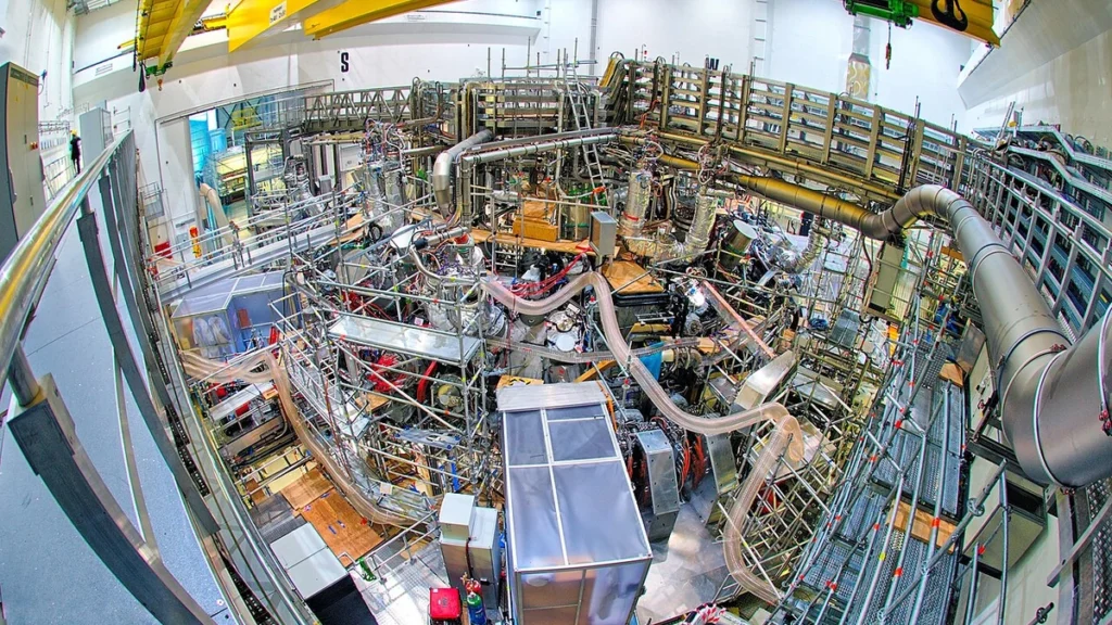Wide-angle overhead view of the Wendelstein 7-X stellarator inside its torus hall in Greifswald, Germany.