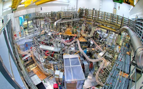 Wide-angle overhead view of the Wendelstein 7-X stellarator inside its torus hall in Greifswald, Germany.