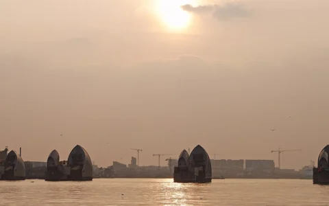 Thames Barrier flood gates on the River Thames in London beneath a sunlit sky.