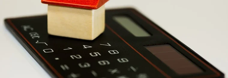 Household budgeting concept with a small home model on a calculator.