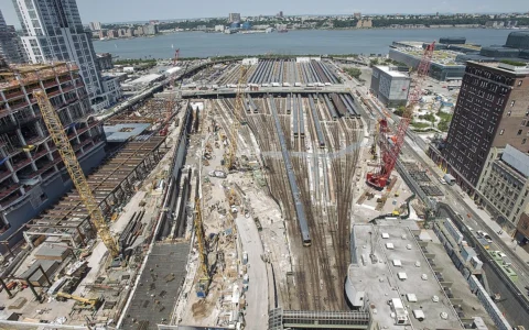 Construction activity at Hudson Yards in Manhattan with cranes, rail yard tracks and surrounding buildings.