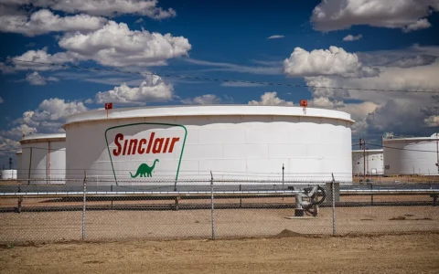 White Sinclair crude oil storage tanks behind a fence at the HF Sinclair refinery in Wyoming.