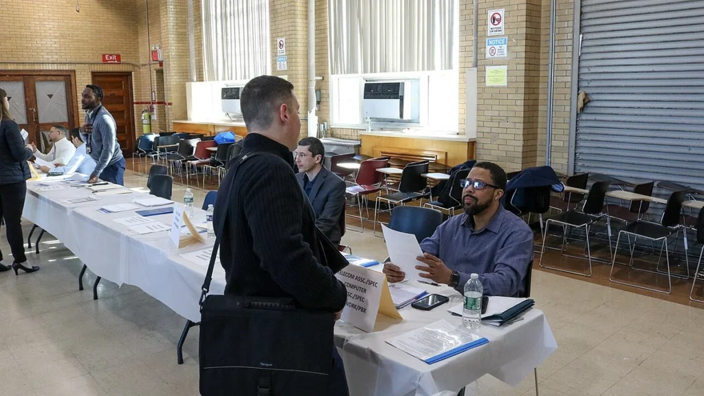Job applicant speaking with a recruiter across a table at a New York City Transit job fair in Brooklyn.