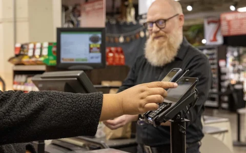 A shopper holds a mobile phone to a payment terminal as a cashier stands at a grocery store checkout in Seattle.