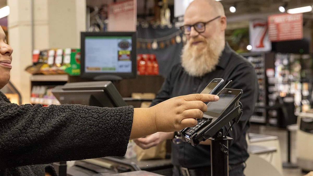 A shopper holds a mobile phone to a payment terminal as a cashier stands at a grocery store checkout in Seattle.