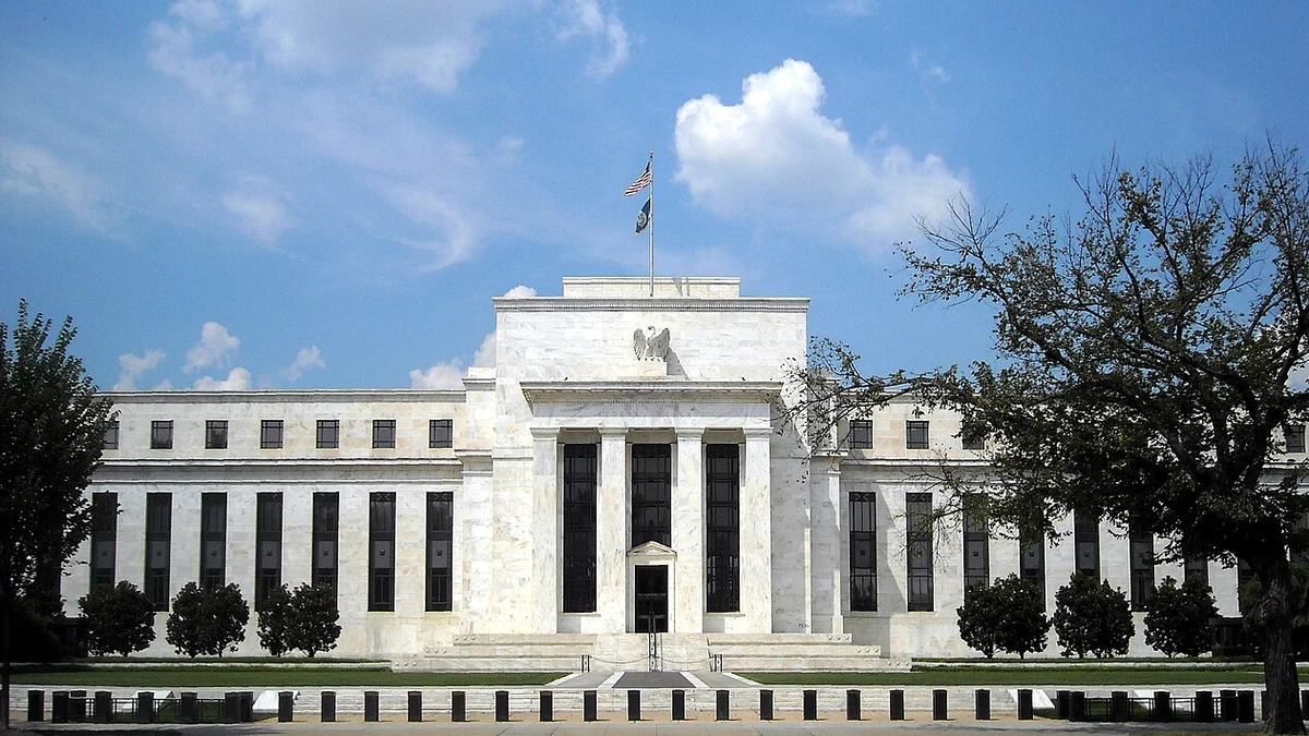 Front of the Marriner S. Eccles Federal Reserve Board Building in Washington, D.C., with trees and a blue sky.