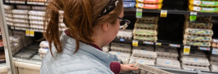 Grocery store employee scanning a carton of eggs with a handheld device in a Seattle supermarket.