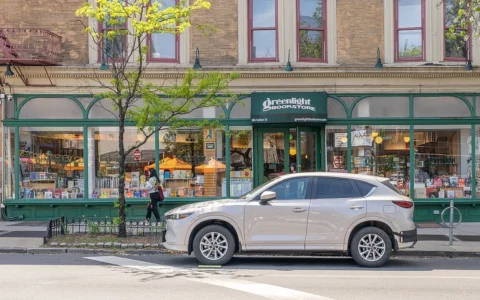 Exterior of Greenlight Bookstore in Brooklyn, with books visible in the front windows and a vehicle parked outside.