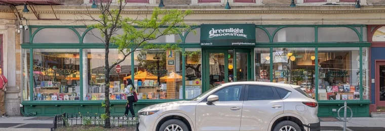 Exterior of Greenlight Bookstore in Brooklyn, with books visible in the front windows and a vehicle parked outside.