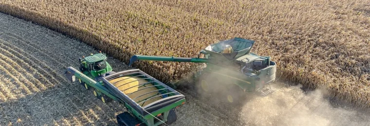 Aerial view of a combine harvester unloading yellow corn into a green grain cart during harvest in Minnesota.