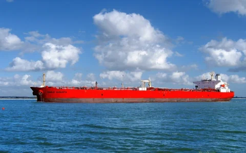 Red-hulled Eagle Augusta crude-oil tanker passing through waters near the Houston Ship Channel under a cloud-filled sky.