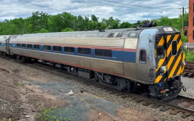 Southbound Amtrak Hartford Line train led by cab car 9647 passing through downtown Windsor Locks, Connecticut, in June 2025.