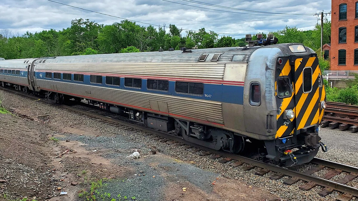 Southbound Amtrak Hartford Line train led by cab car 9647 passing through downtown Windsor Locks, Connecticut, in June 2025.