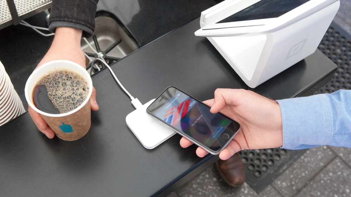 A customer holds an iPhone beside a Square contactless payment reader while buying coffee.